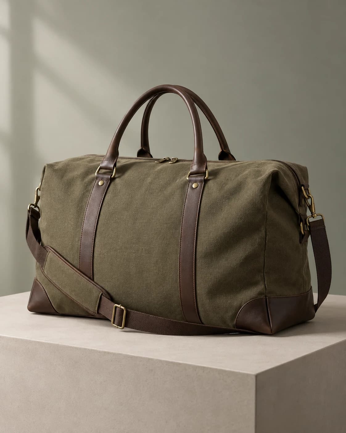 a foldable olive canvas weekender bag in a matte neutral plinth, a front three-quarter product view with large diffused side light